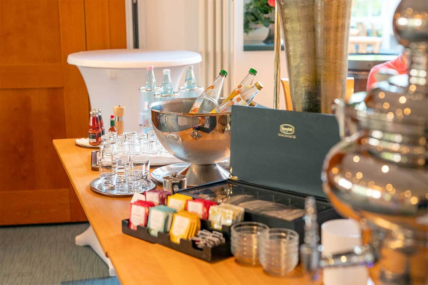 A bar area with a large metal bowl, glasses, bottles, and a laptop.