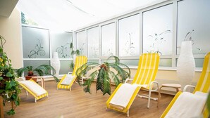 A sunlit room with wooden flooring, yellow-striped lounge chairs, and large windows with abstract designs. - Waldhotel Schäferberg (Espenau)