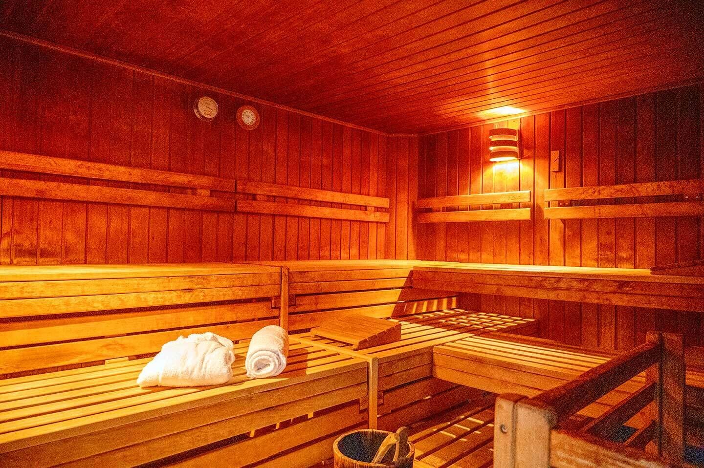 A sauna with wooden benches, a bench heater, and a towel rack.