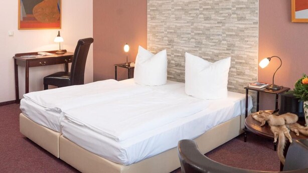 A hotel room with a bed, desk, chair, and a wall with a textured pattern. - Hotel Adagio (Leipzig)