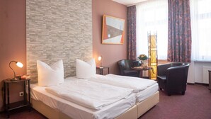 A hotel room with a bed, two bedside tables, a chair, a lamp, and a window with curtains. - Hotel Adagio (Leipzig)
