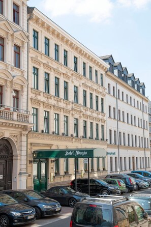 Ein mehrstöckiges Hotel im klassischen Stil, mit einem markanten Eingang und einer grünen Markise mit der Aufschrift 'Hotel Adagio'.
