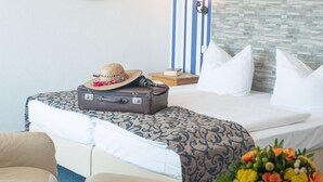 A hotel room with a bed, a suitcase, a hat, a vase with flowers, and a wall with striped wallpaper and pictures. - Hotel Adagio (Leipzig)