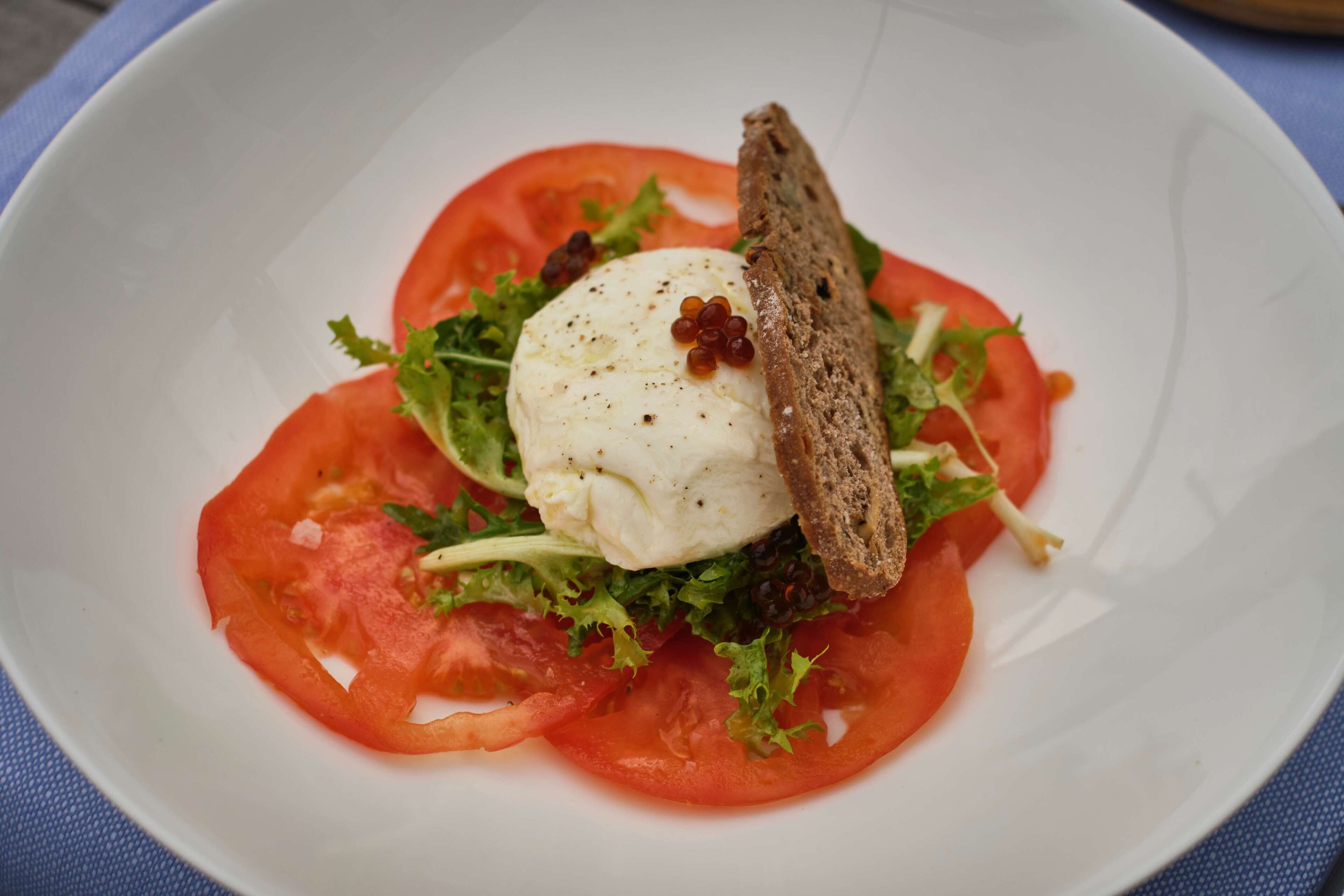Ein Teller mit pochiertem Ei, Tomatenscheiben, Salat und einem Stück Brot.