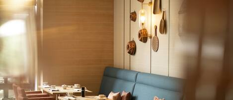 A restaurant with a blue booth seating area, wooden tables, and a wall decorated with various items.