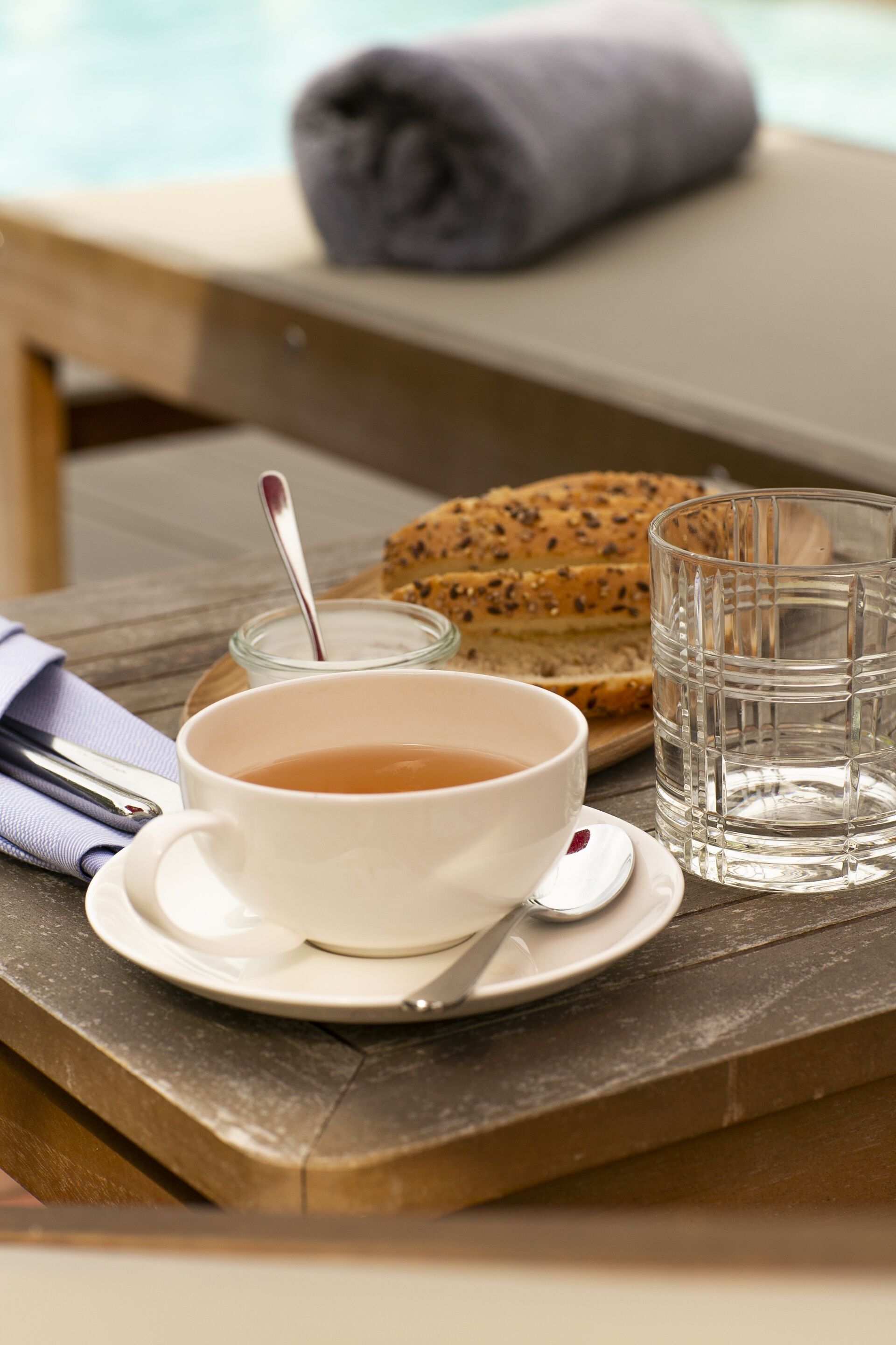 A table with a bowl of tea, a glass of water, a slice of bread, and a spoon.