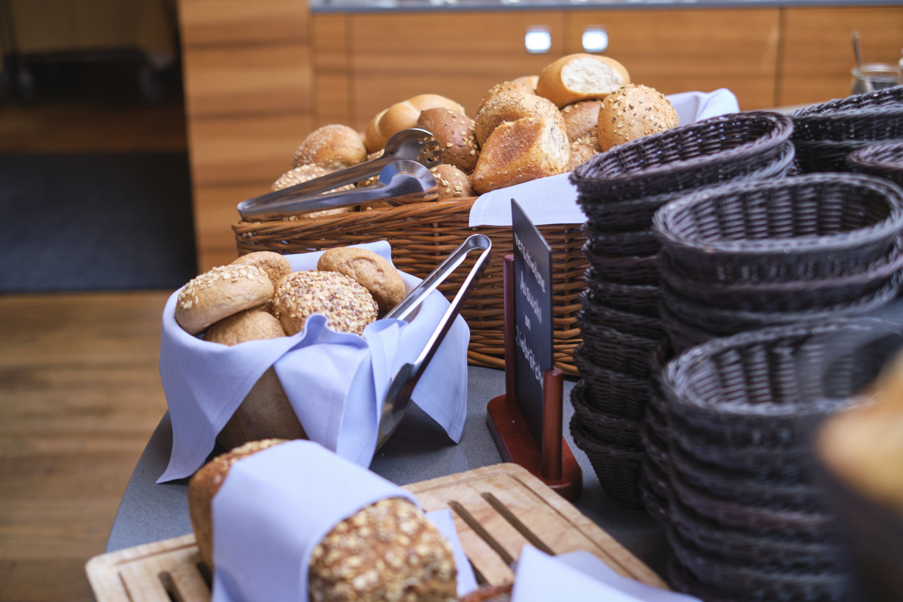 Verschiedene Brotsorten und Gebäckstücke sind auf einer Tischdarstellung arrangiert, zusammen mit Körben und einem Schild, das die Speisekarte anzeigt.