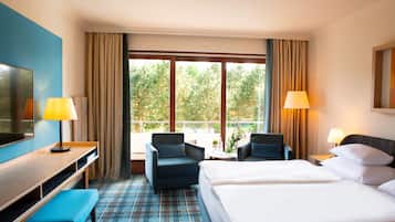 A hotel room with a bed, two armchairs, a desk, a TV, and a balcony with curtains.