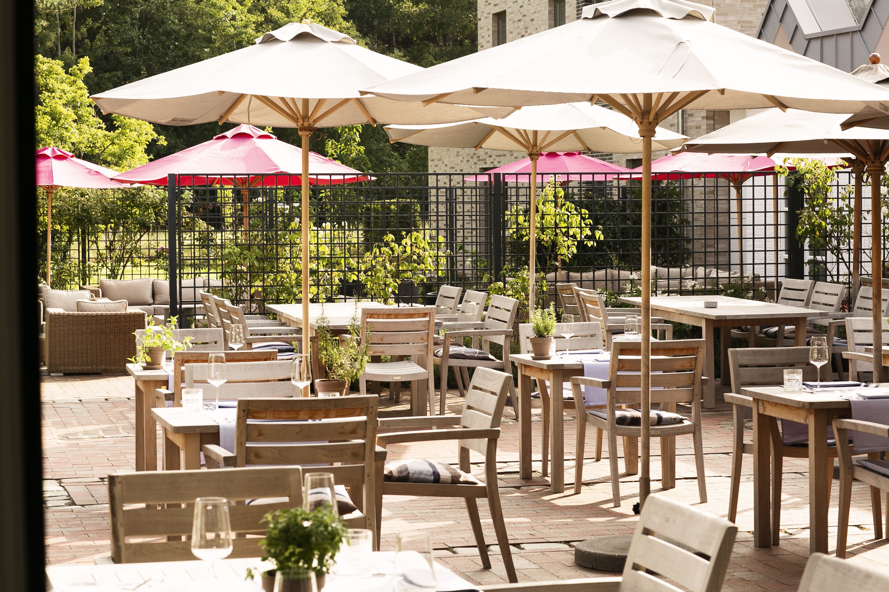 Een terras buiten met houten tafels en stoelen, waarvan sommige onder parasols.