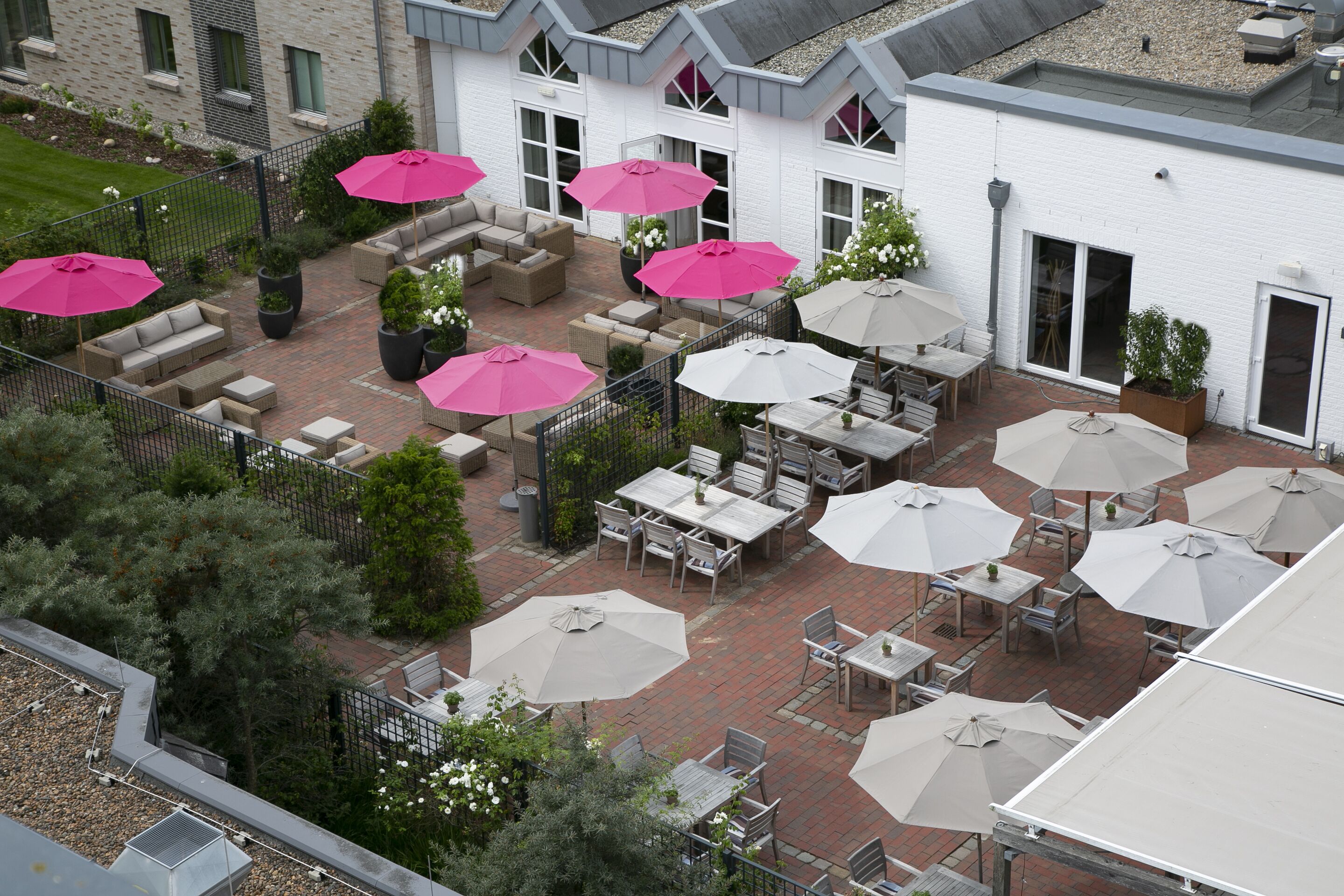 Een terras buiten met verschillende zithoeken, waarvan sommige voorzien zijn van parasols.