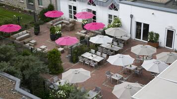 Een terras buiten met verschillende zithoeken, waarvan sommige voorzien zijn van parasols.