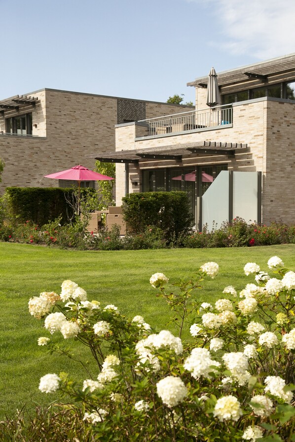 Una casa moderna con fachada de ladrillo, un balcón y un jardín cuidado con flores blancas.