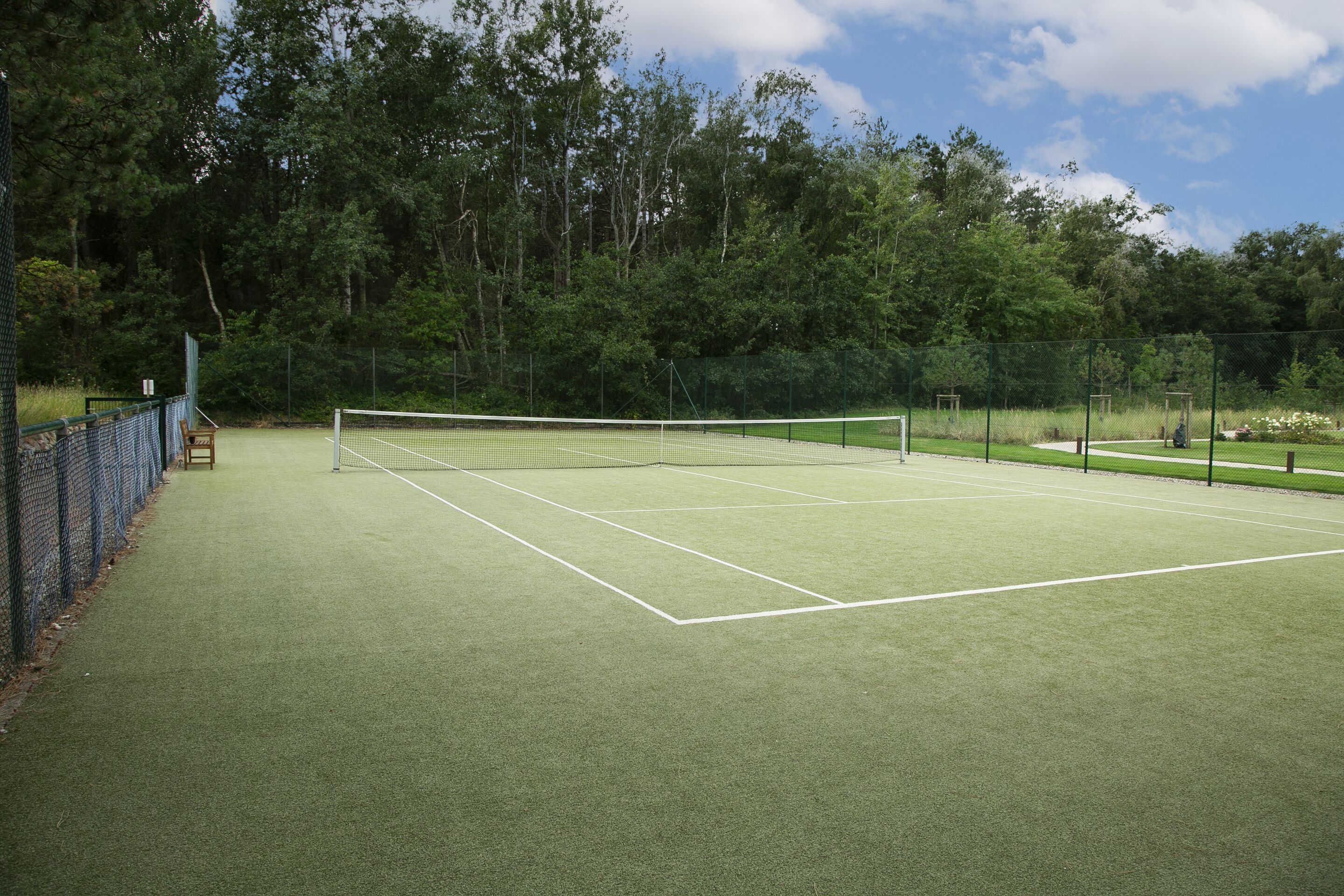 Ein Tennisplatz mit Netz, umgeben von einem Zaun und Bäumen.