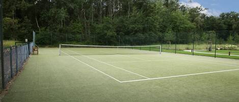 Una cancha de tenis con una red, rodeada por una valla y árboles.