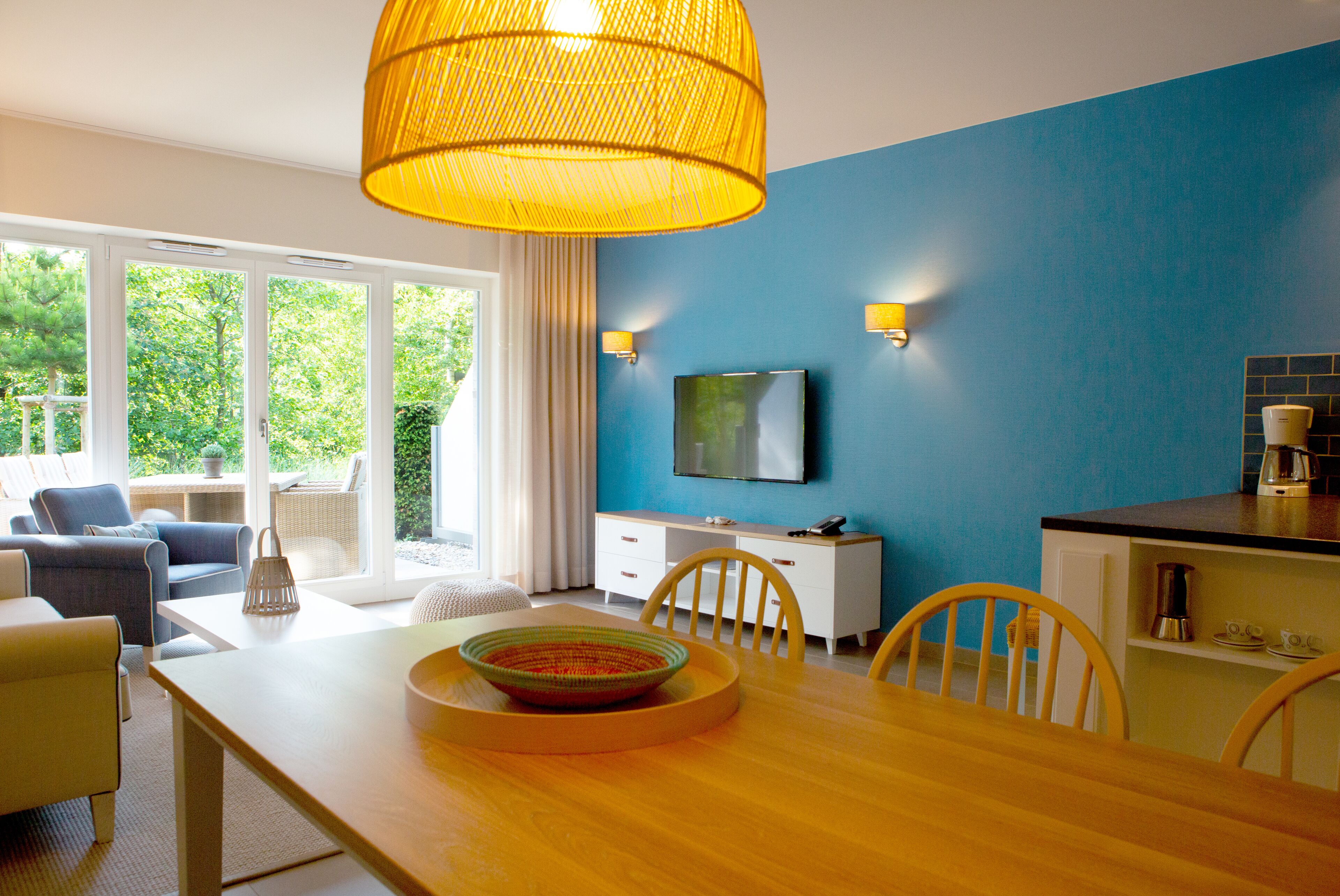 A modern kitchen with a dining area, large windows, and a television.