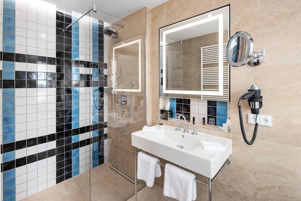 Un baño moderno con cabina de ducha de vidrio, un espejo grande y un lavabo blanco.