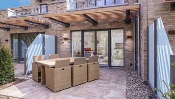 Ein modernes Haus mit einer Terrassenfläche, die Korbmöbel und eine Glastür zu einem Innenbereich zeigt.