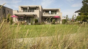 Une maison moderne à deux étages, dotée d’une pelouse bien entretenue et de deux parasols rouges.