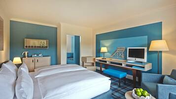 A hotel room with a large bed, a desk with a TV, a chair, and a small table with apples.