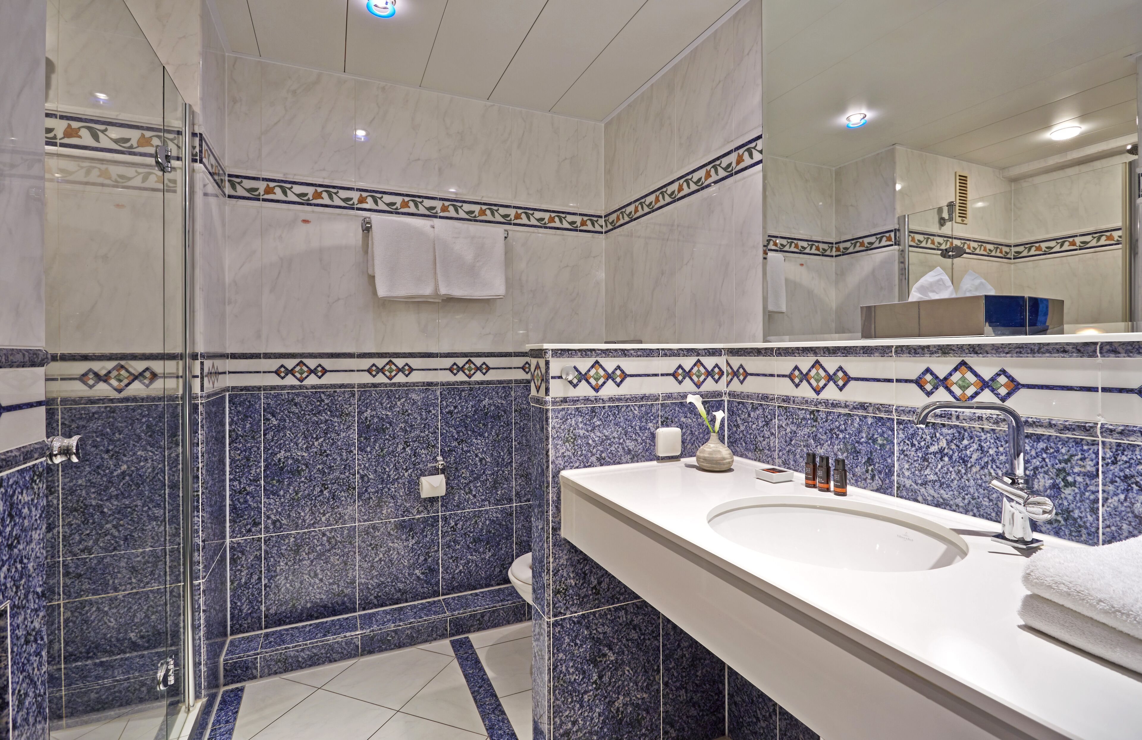 A modern bathroom with a glass shower enclosure, a white sink with a mirror, and decorative blue and white tiles.