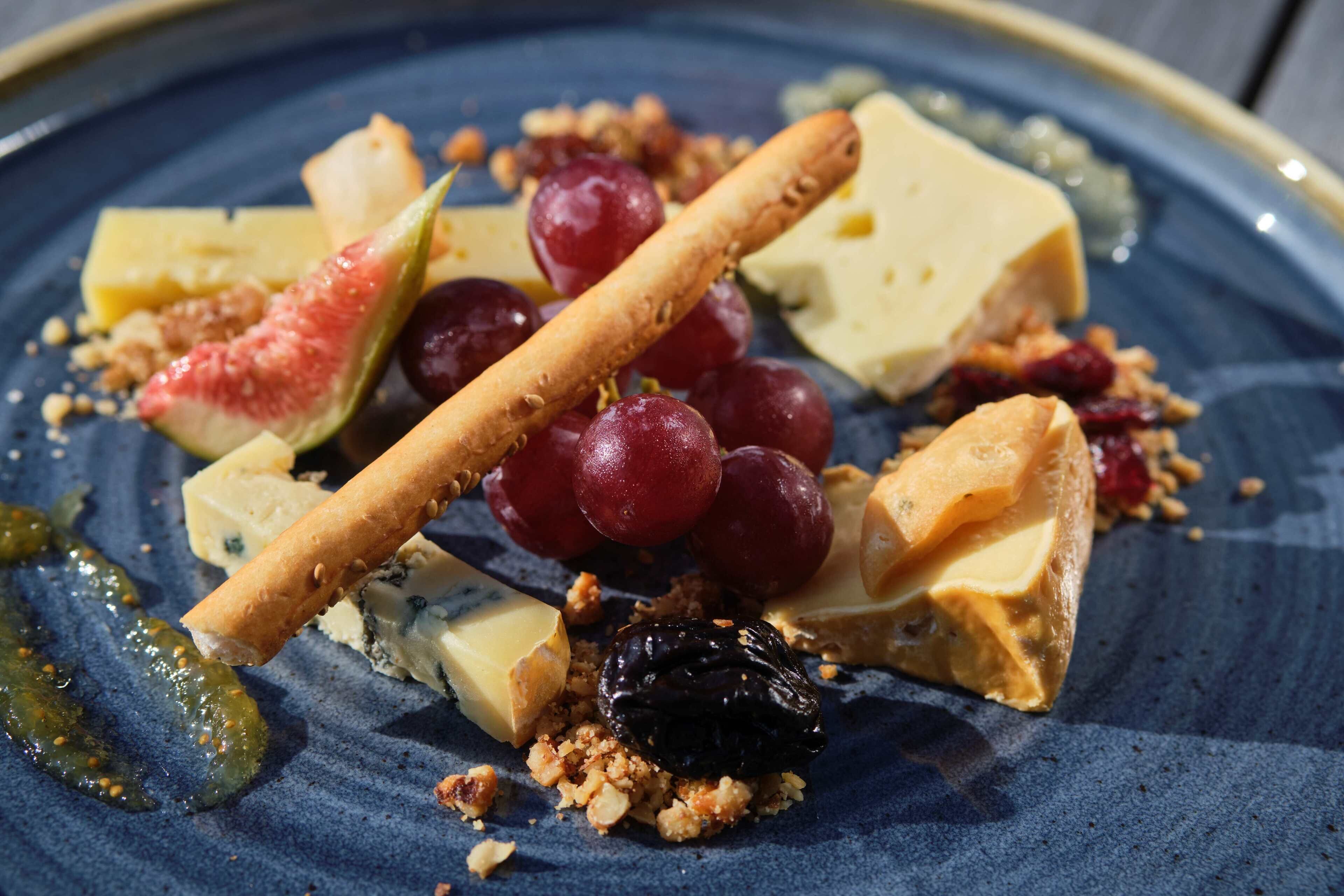 Una tabla con varios quesos, uvas, una rama de canela y frutos secos.