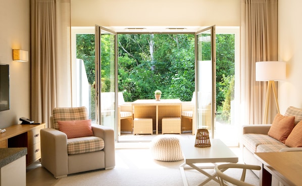 Una habitación de hotel moderna con sofá, sillón y una mesa de comedor con sillas.