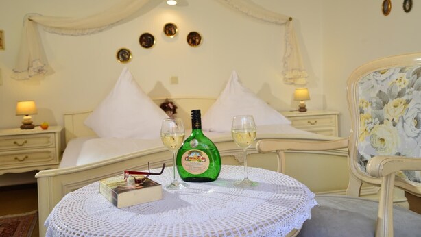 Een keurig opgemaakt slaapkamer met een bed, een nachtkastje met een lamp, een ronde tafel met een boek en glazen, en een stoel met een bloemenprint.
