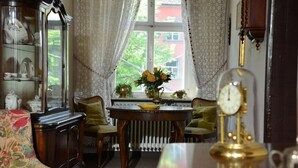 Een gezellige kamer met een houten tafel, stoelen, een radiator en een raam met gordijnen.
