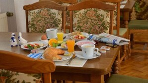 Een ontbijttafel met borden eten, een croissant, een kop koffie en een krant.
