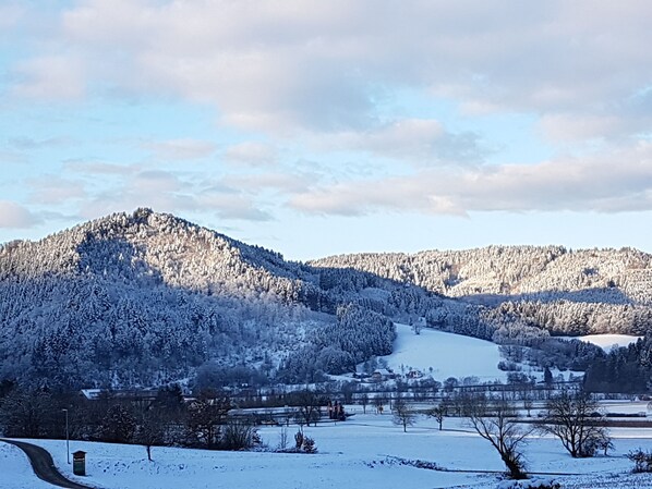 A snow-covered landscape with a winding road and a mountain in the background.