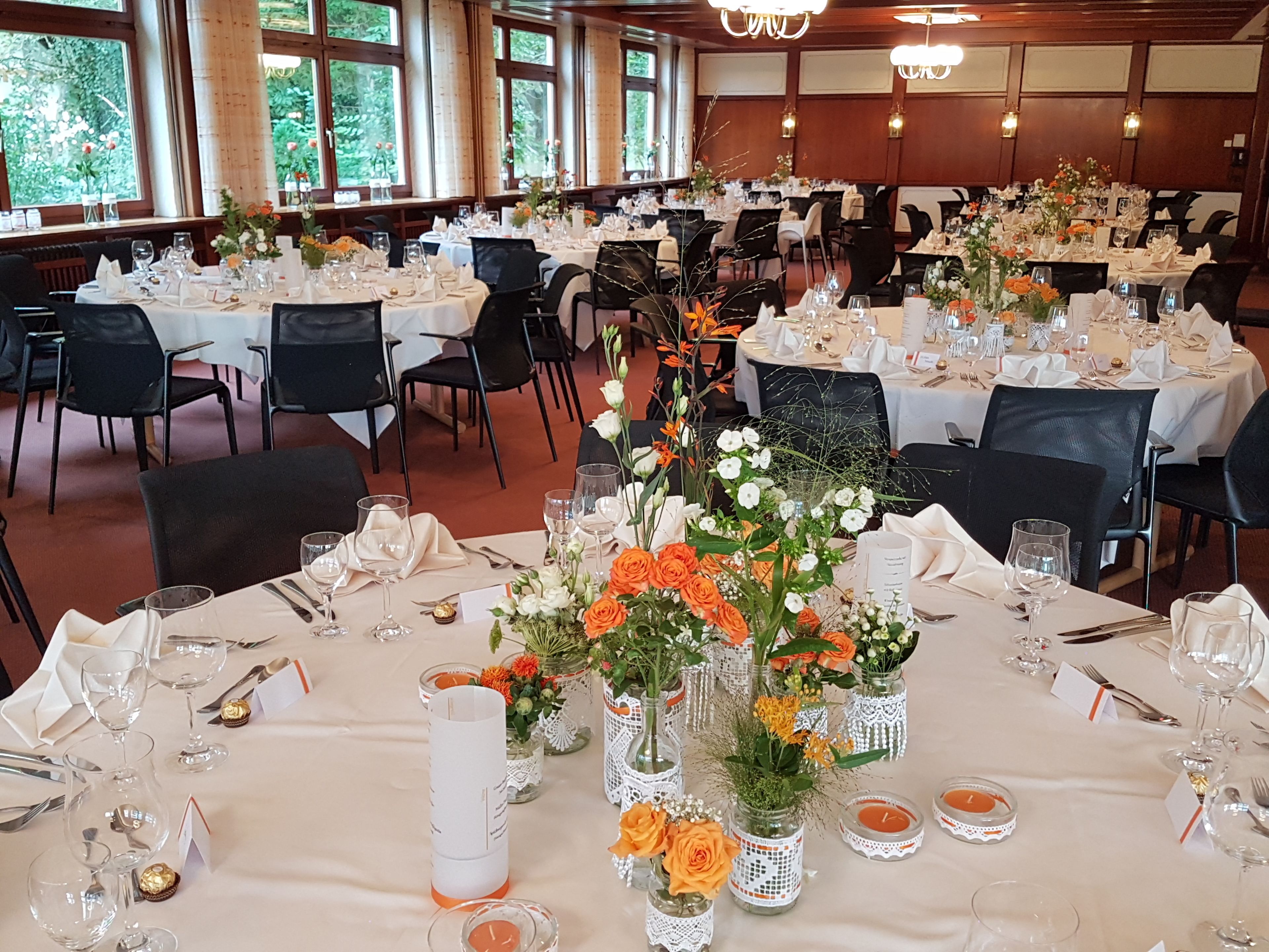 Een balzaal met gedekte tafels voor een formeel evenement, met bloemstukken en kandelaars.