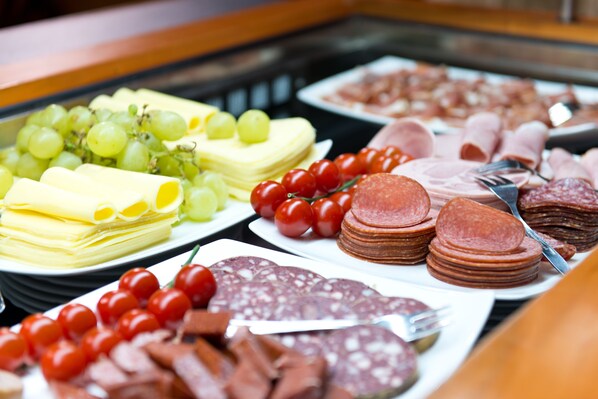 A buffet with various food items including cheese, grapes, cherry tomatoes, and different types of meat.