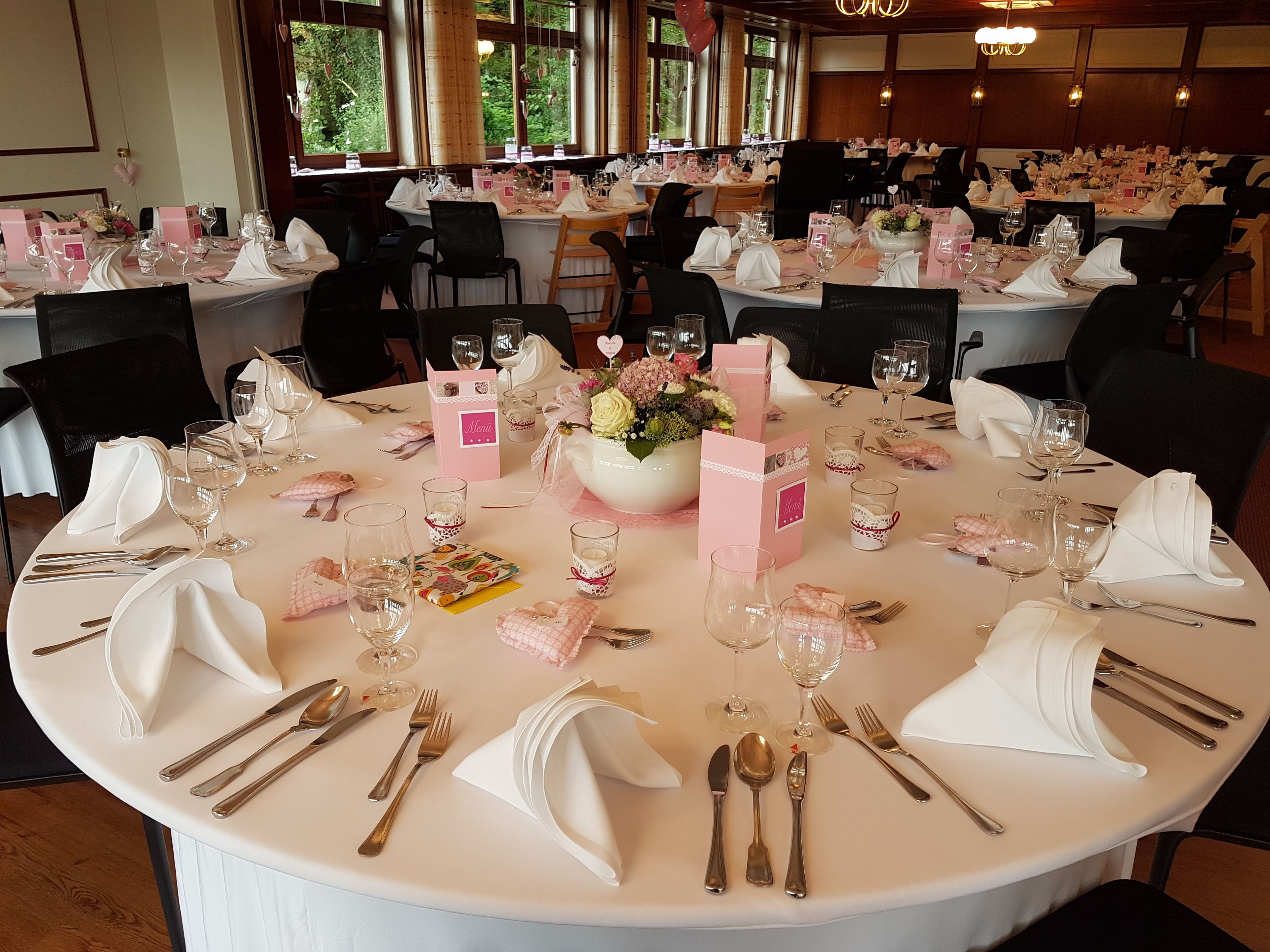A round dining table set for a formal event, with multiple place settings, glasses, and a centerpiece.