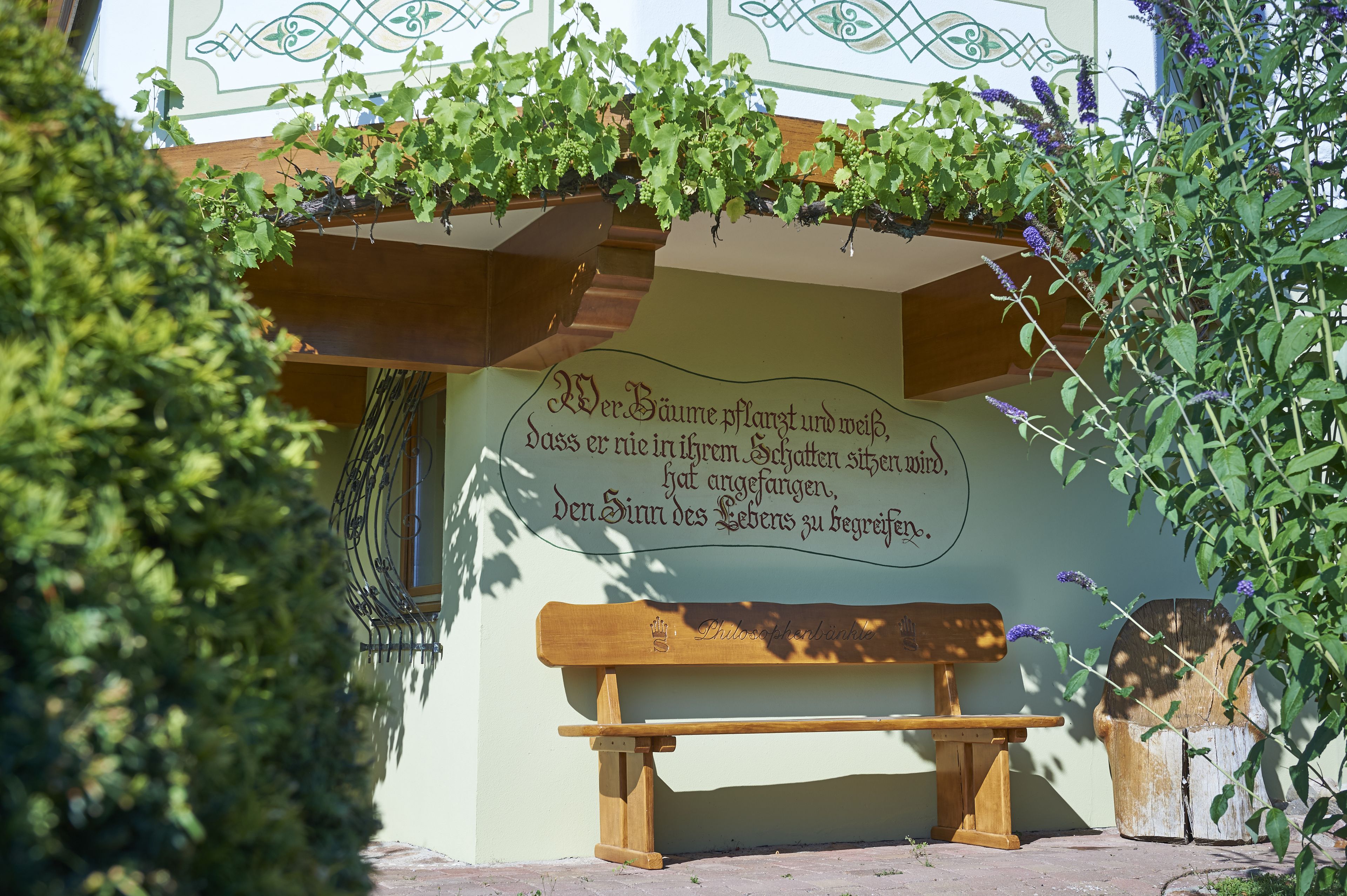 A wooden bench with a plaque in front of a wall with a decorative design.