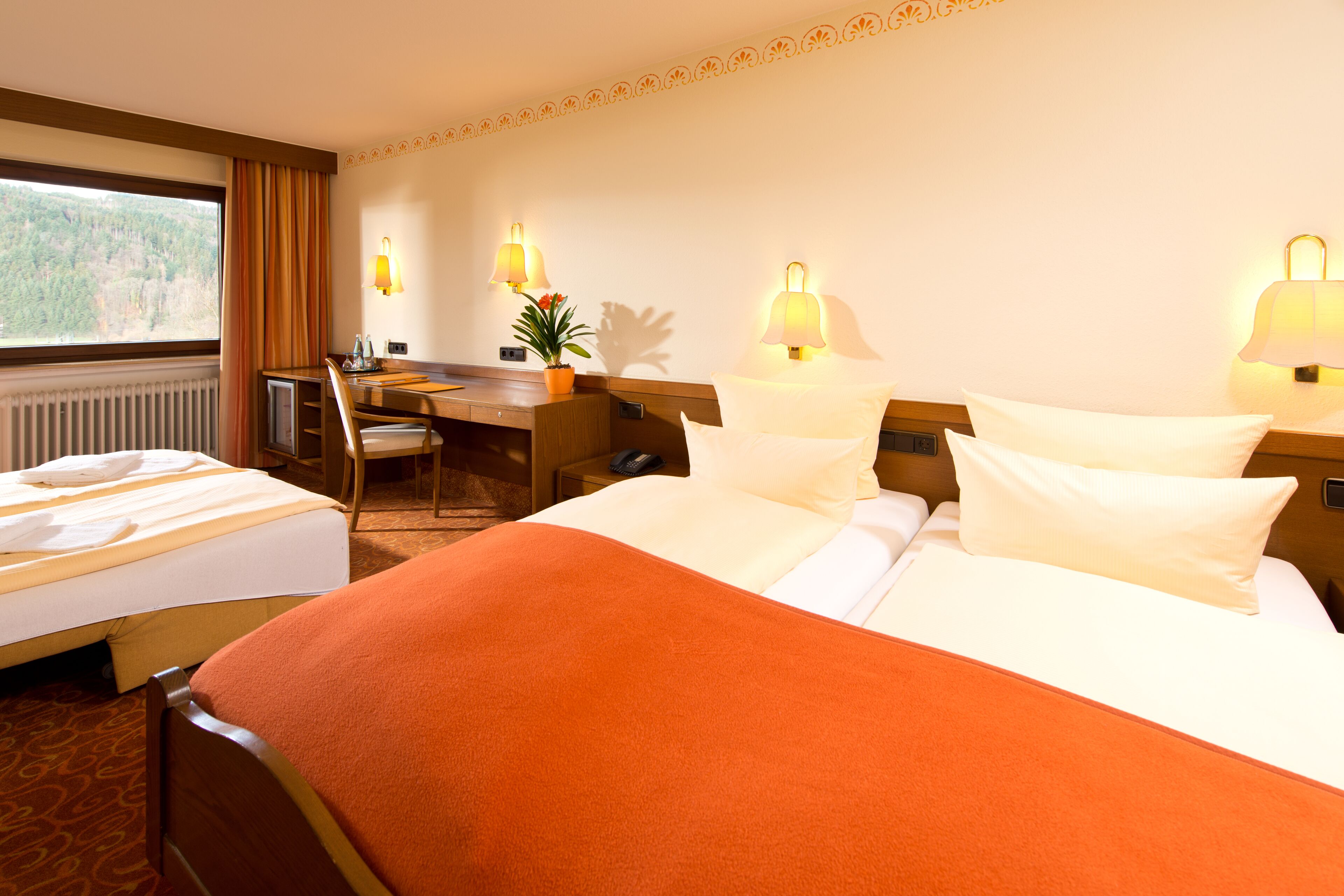 Ein Hotelzimmer mit zwei Betten, einem Schreibtisch, einem Sessel und zwei Wandlampen.