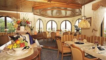 A dining area with wooden furniture, a fruit and vegetable centerpiece, and large arched windows.