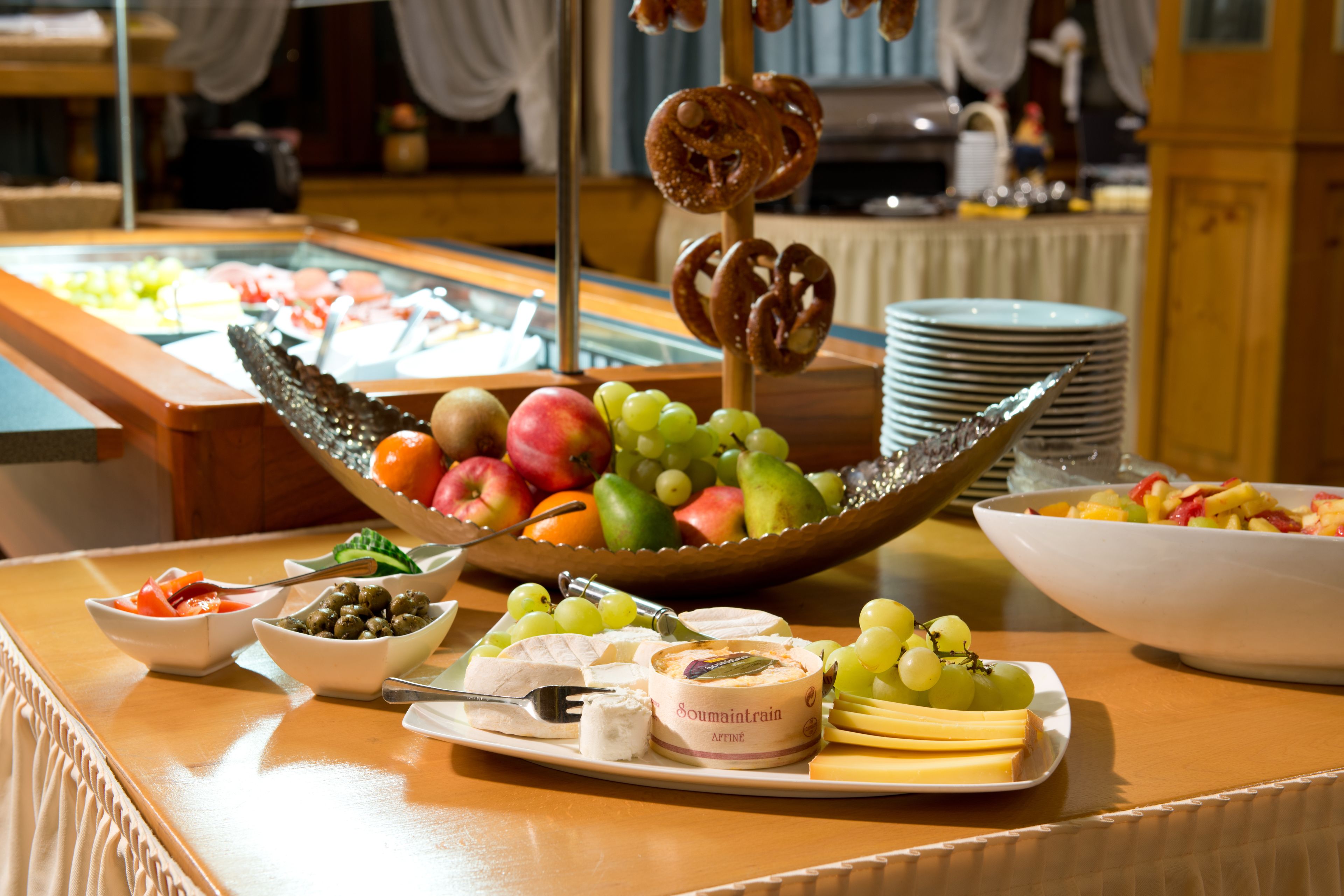 Une table de buffet proposant divers aliments, notamment des fruits, des fromages et un bol de bretzels.