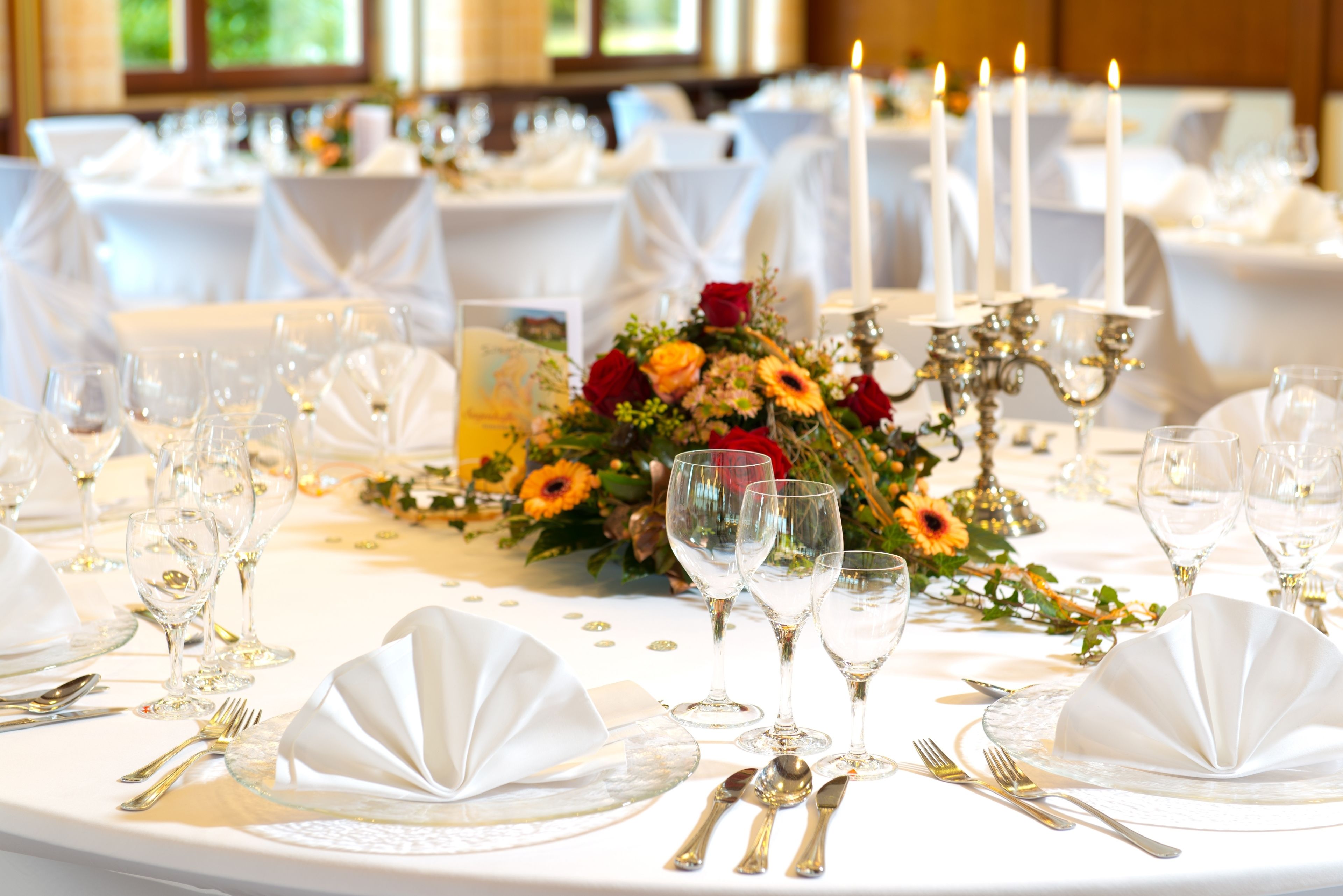 Une table ronde dressée pour un événement formel, avec des nappes blanches, de la verrerie et un centre de table composé de fleurs.