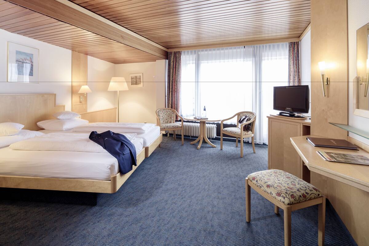 A hotel room with two beds, a desk, a chair, a television, and a window with curtains.
