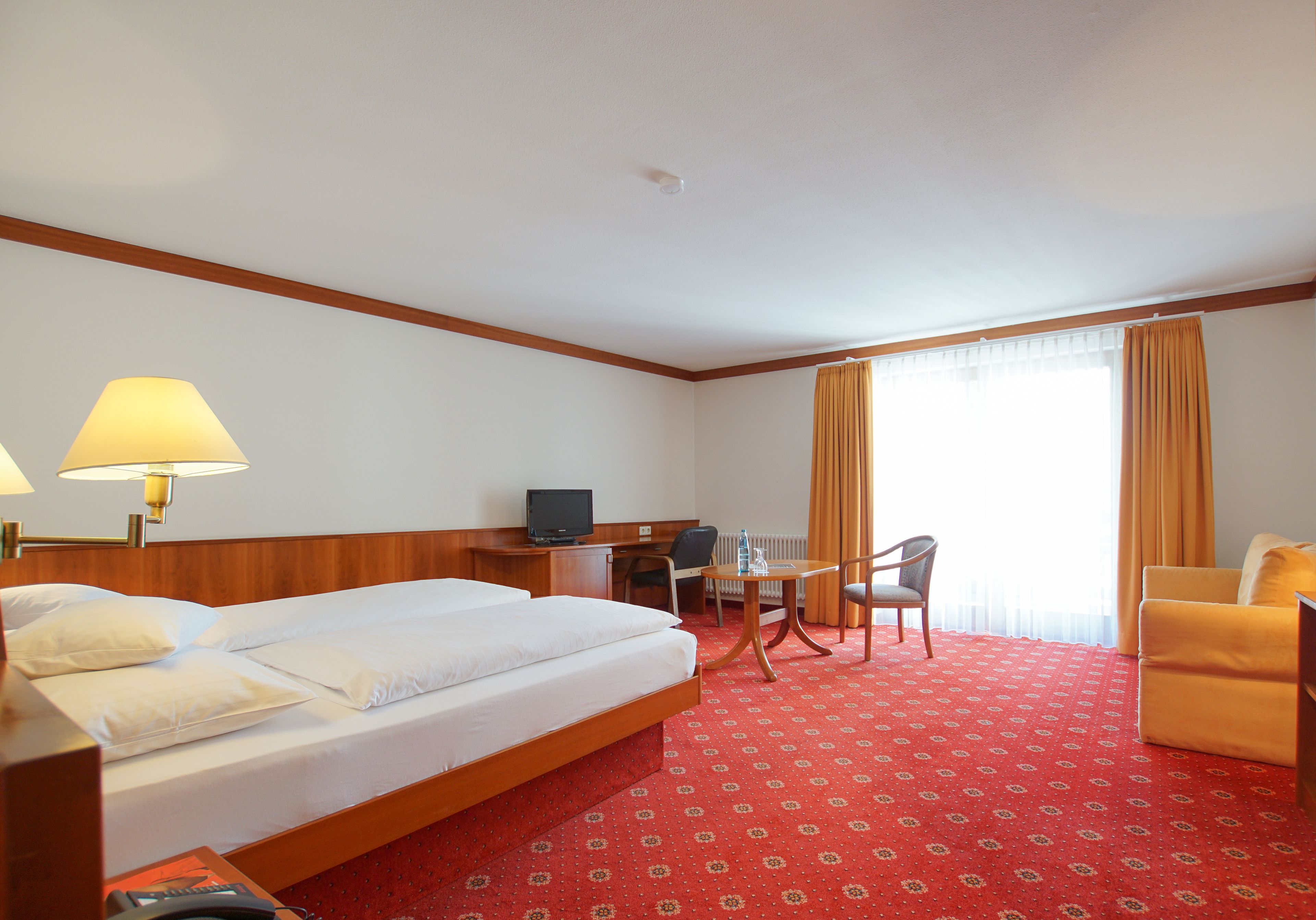 Une chambre d’hôtel équipée d’un lit, d’un bureau, d’une chaise, d’une télévision et d’une fenêtre avec des rideaux.
