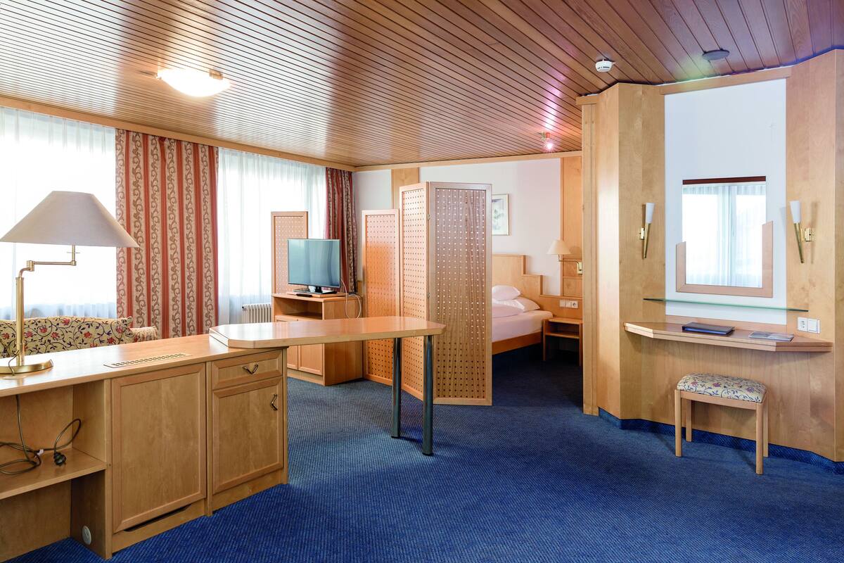 A hotel room with a wooden desk, a television, a bed, and a small seating area.