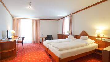 Ein Hotelzimmer mit einem großen Bett, einem Schreibtisch, einem Stuhl, einem kleinen Tisch und einem Fenster mit Vorhängen.