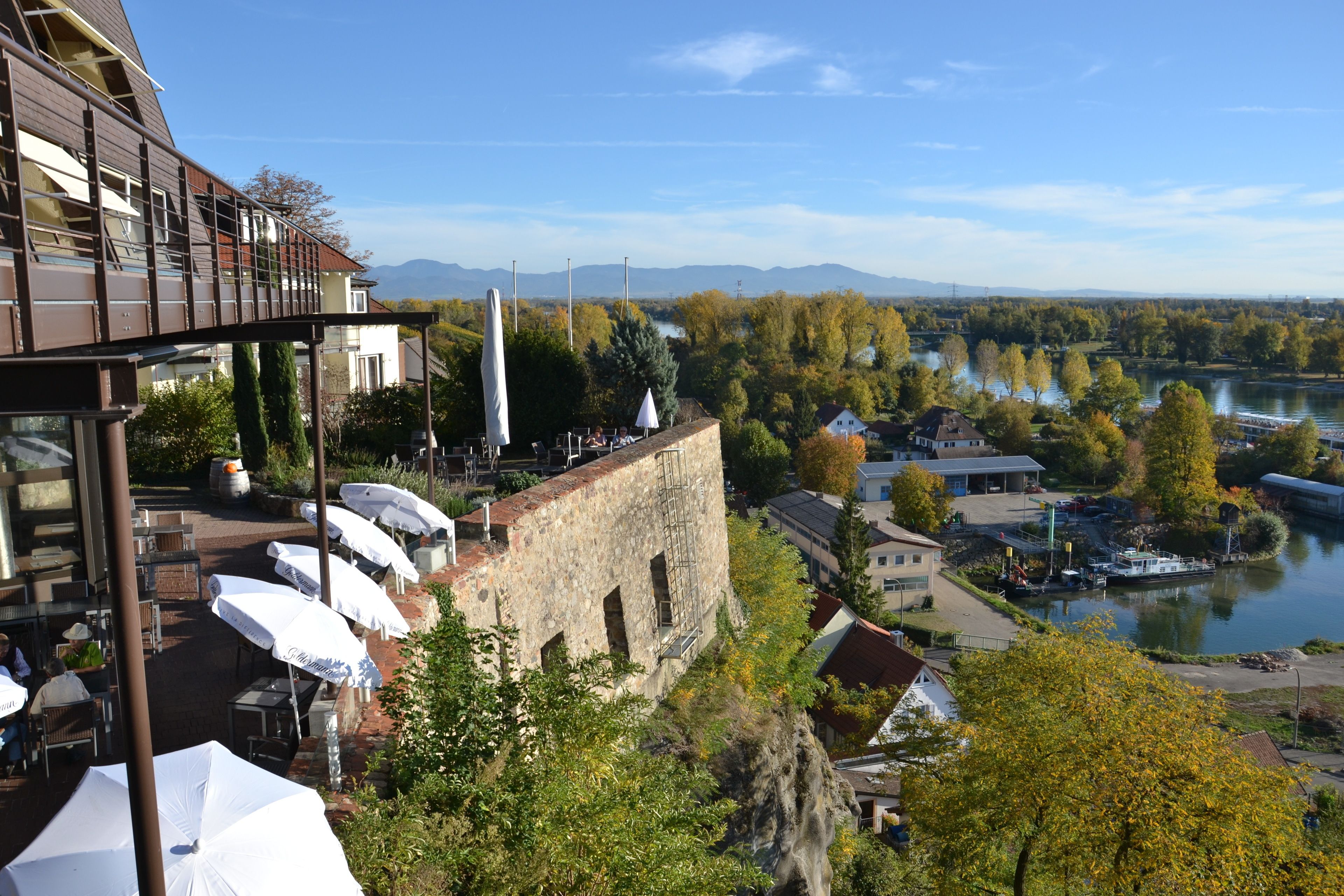 A riverside view with outdoor seating, stone buildings, and a boat dock.