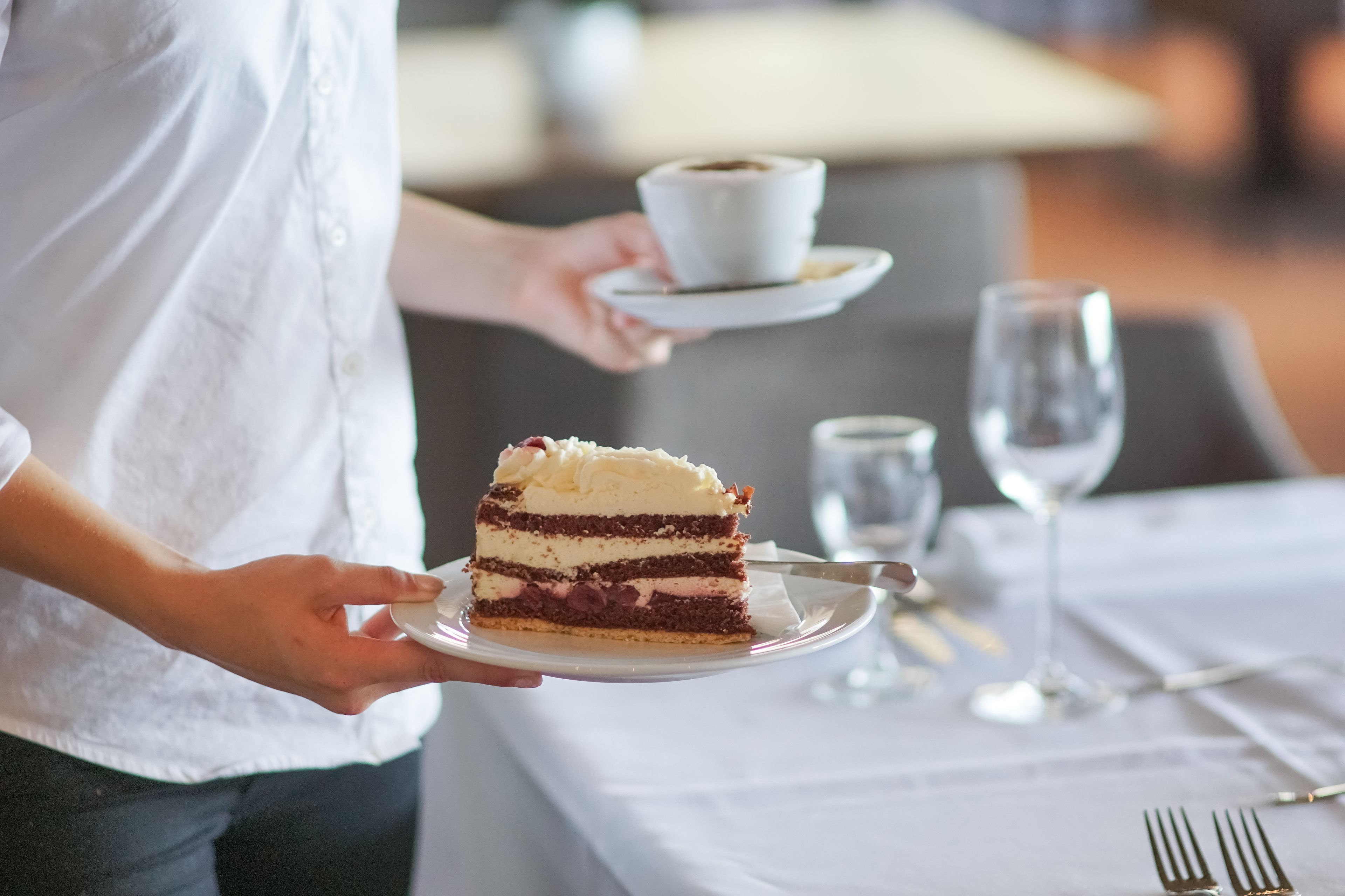A person serving a slice of layered cake on a white plate.
