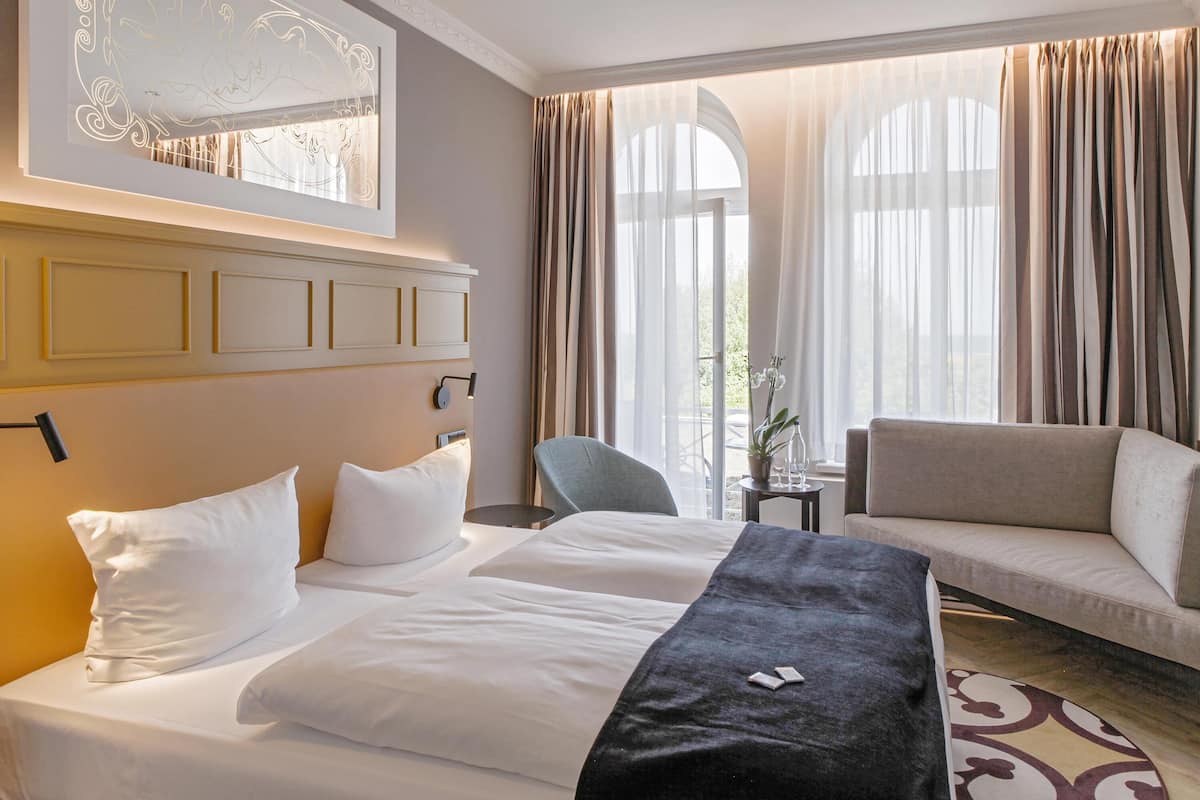 A hotel room with a bed, a sofa, a chair, and a large window with curtains.