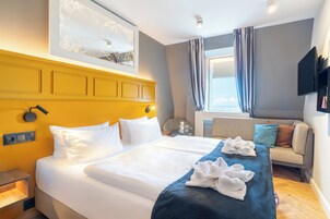 Habitación de hotel con una cama grande, un sofá, un televisor y una ventana con cortinas.