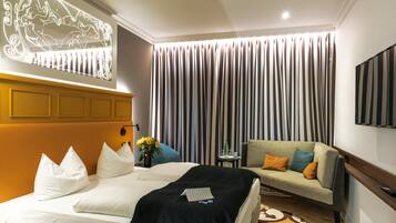 A hotel room with a large bed, a sofa, a flat-screen TV, and a decorative wall piece.