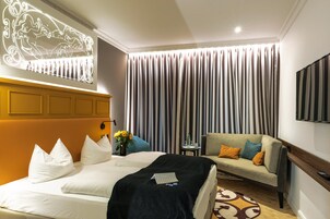 A hotel room with a large bed, a sofa, a flat-screen TV, and a decorative wall piece.