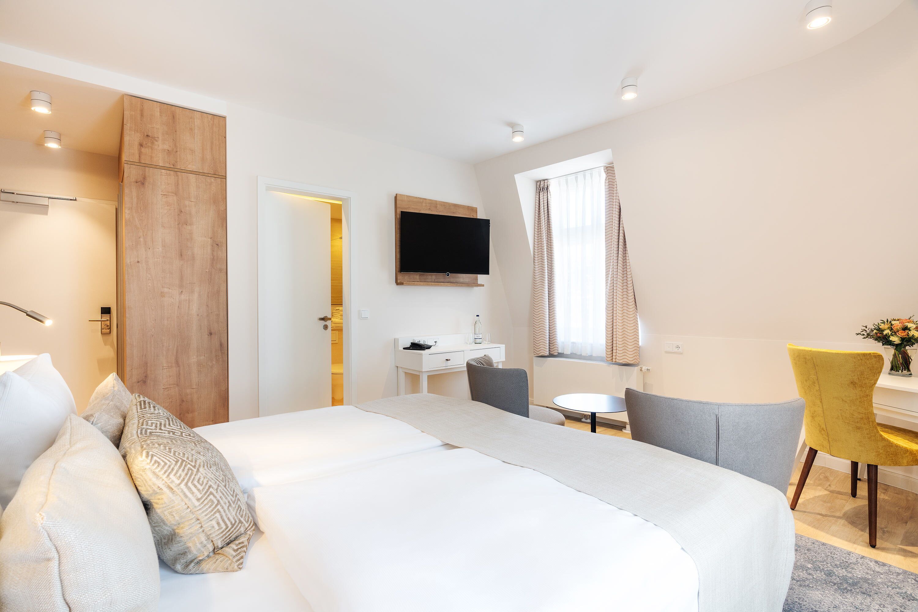A hotel room with a bed, a desk, a chair, a TV, and a window with curtains.