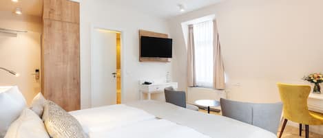 A hotel room with a bed, a desk, a chair, a TV, and a window with curtains.